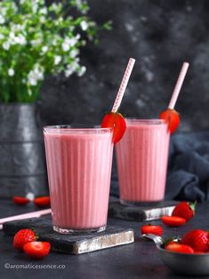 two glasses filled with pink smoothie on top of a black table next to strawberries