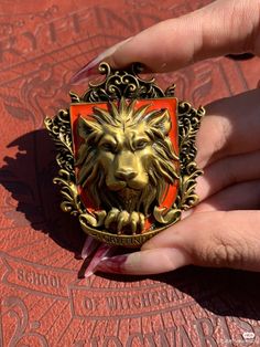 a woman's hand holding an orange and gold lion head broochle on top of a red surface