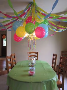 a green table topped with lots of balloons and streamers hanging from it's ceiling