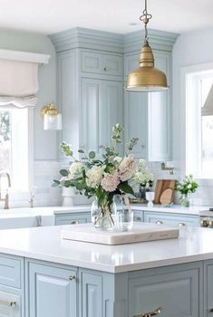 a kitchen island with flowers in a vase on the top and gold pendant light hanging over it