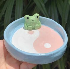 a small toy frog sitting on top of a pink and blue bowl filled with liquid