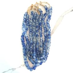 three strands of blue glass beads on a white marble surface with gold clasps and string