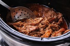 the meat is being cooked in the slow cooker with a ladle to stir it