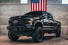 a black truck parked in front of a brick wall with an american flag on it