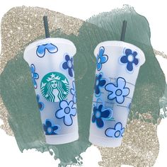 two starbucks cups with blue flowers on them are next to glittery green and silver background