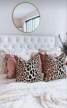 a white bed topped with lots of pillows next to a round mirror on the wall