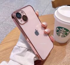 a person holding an iphone in their hand next to a cup of coffee and a starbucks drink