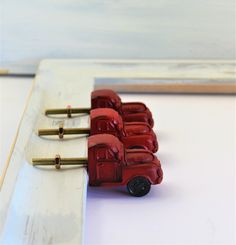 three red toy trucks are lined up on a white board with screws in the middle