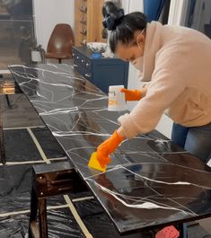 a woman is painting a black table with white paint and orange sponges on it