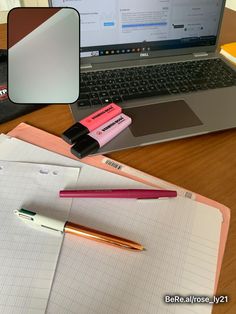 an open laptop computer sitting on top of a wooden desk next to a notebook and pen