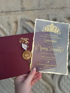 a person holding up a red and gold wedding card with a wax stamp on it