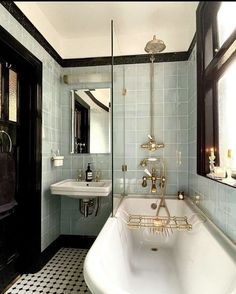 a bath tub sitting next to a sink in a bathroom under a window with black and white tiles