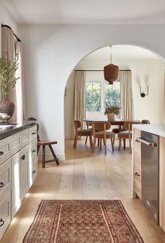 an archway leading into a dining room and kitchen with white cabinets, wood floors and wooden chairs