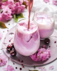 two glasses filled with liquid sitting on top of a plate next to flowers and cherries