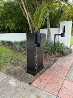 a tall black box sitting on the side of a road next to a palm tree