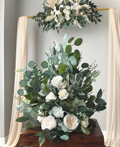 a bouquet of white flowers and greenery on a table in front of a curtain