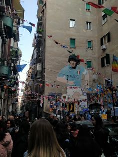 a crowd of people walking down a street next to tall buildings with flags on them