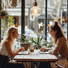 two women sitting at a table with laptops in front of them, both looking at each other