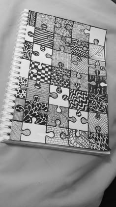 a black and white photo of a notebook with many different designs on the cover, sitting on a bed