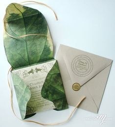 an envelope and some green leaves on a white table