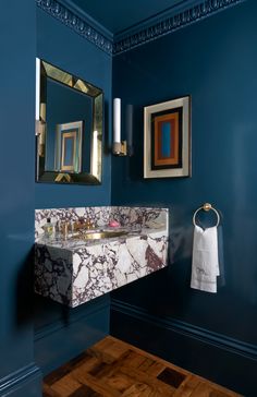 a bathroom with blue walls and marble counter top, gold framed mirror above the sink