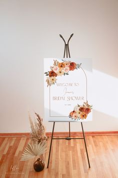 a welcome sign with flowers on it in front of a white wall and wooden floor