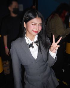 a woman in a suit and bow tie making the peace sign with her hand while standing next to other people