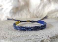 Narrow hand loomed fiber bracelet in indigo blue shades with golden sparkle.   Woven with silk, cotton and metallic thread. The warp yarn is durable linen in navy blue. Tiny brass beads at the ends of the ties. This is a slim but sturdy weaving that reminds of Lapis Lazuli - different beautiful blue shades with shimmering spots of gold. Simple, textile, minimalist. Width: 7 mm / 0.27'' Woven length: 13 cm / 5.1'' Wrist size easily adjustable with a macrame slipknot closure. Carefully woven and w Blue Woven Bracelets As A Gift, Blue Woven Bracelets As Gifts, Blue Woven Bracelet Perfect For Gifting, Handwoven Blue Bracelet Gift, Blue Woven Bracelet Perfect For Gift, Blue Woven Friendship Bracelets For Festivals, Blue Woven Braided Bracelets For Festival, Blue Woven Braided Bracelet For Festivals, Golden Sparkle