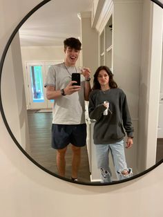 a man and woman standing in front of a mirror taking a selfie with their cell phone