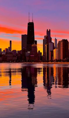 the city skyline is reflected in the water at sunset, with pink and orange clouds