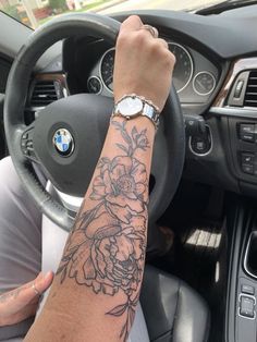 a person with a flower tattoo on their arm behind the steering wheel of a car