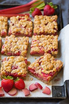 strawberry crumble bars on a baking sheet with strawberries and rhubarb