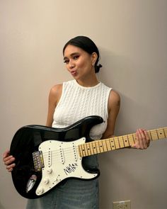 a woman holding an electric guitar in front of her face and posing for the camera