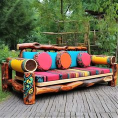 a couch made out of logs with colorful cushions on the top and bottom, sitting on a wooden deck in front of some trees