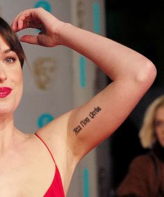 a woman with a tattoo on her arm is posing for the camera while wearing a red dress