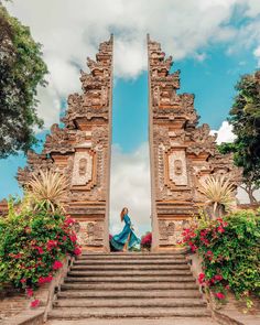 a woman is sitting on the steps leading up to an ornate gate with flowers and greenery