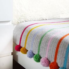 a white bed topped with a colorful blanket and pom poms on top of it