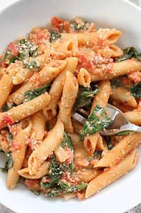 a white bowl filled with pasta and spinach covered in sauce on top of a table