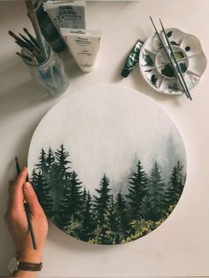 someone is painting a forest scene on a white surface with paintbrushes and watercolors