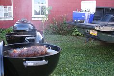 two bbq grills sitting next to each other in the grass near a red building