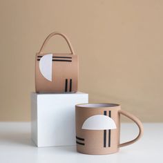 two coffee mugs sitting next to each other on top of a white box,