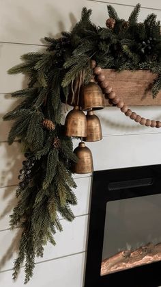 a christmas wreath hanging on the wall next to a fireplace with bells and pine cones