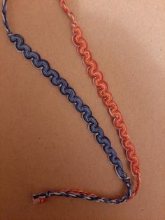 two different colored chains on a brown surface next to an orange and blue string with a black end