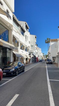 cars are parked on the side of an empty street in front of buildings and palm trees