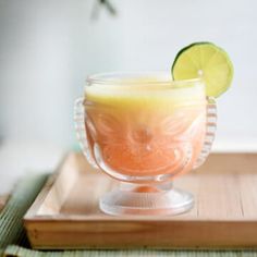 a drink in a glass sitting on top of a wooden tray next to a lime slice