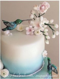 there is a white cake with blue frosting and flowers on the top, along with two hummings