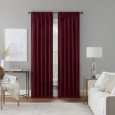 a living room with a couch, chair and window covered in red curtain panels next to a white rug