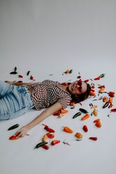 a woman laying on the ground surrounded by chili peppers scattered around her and looking up