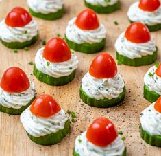 cucumbers with tomatoes and cream cheese on them are arranged on a wooden board