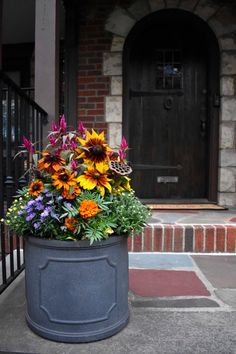 a large flower pot sitting on the sidewalk in front of a door with flowers growing out of it